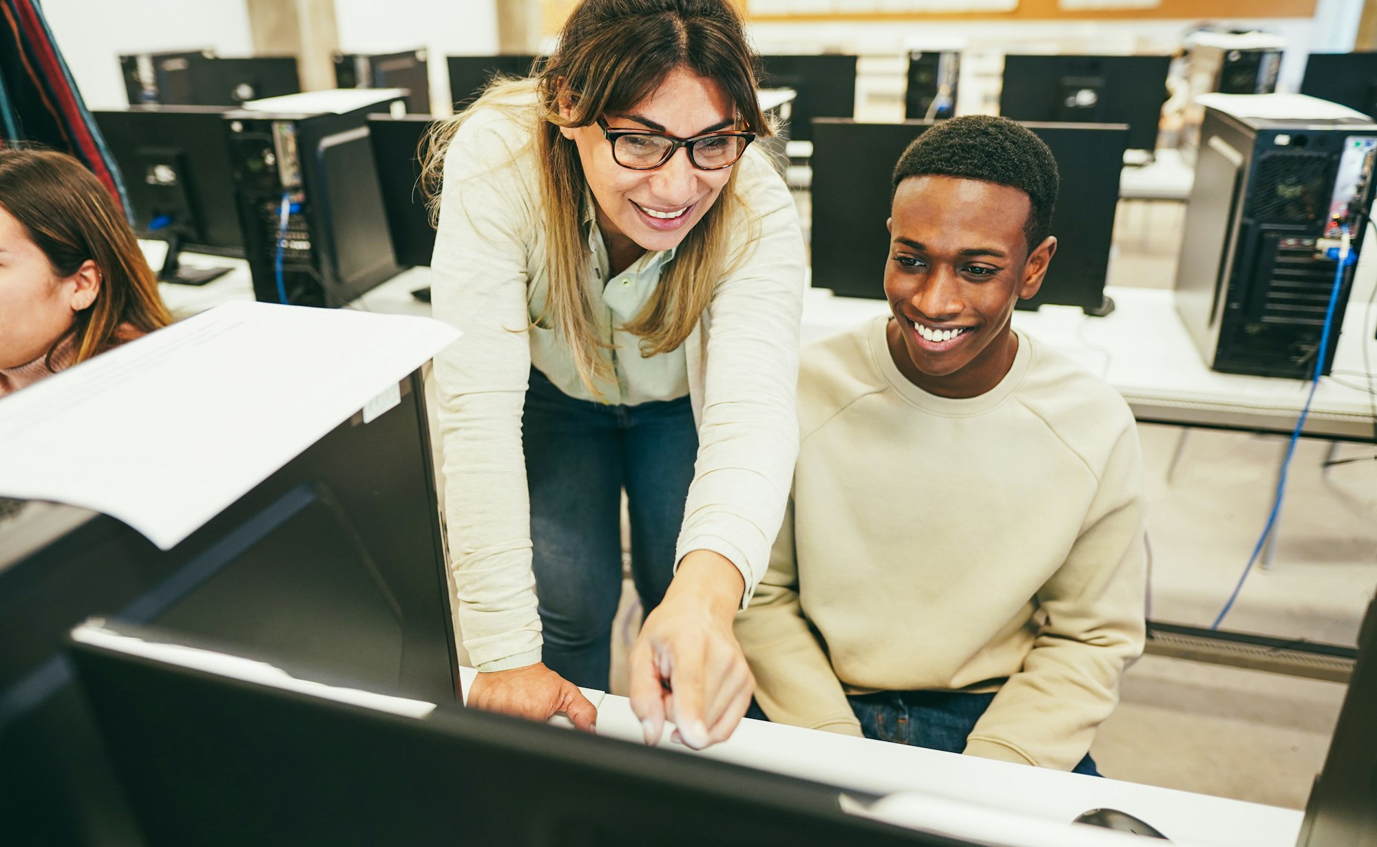 Young student learning how to use personal computer with his teacher at IT college class